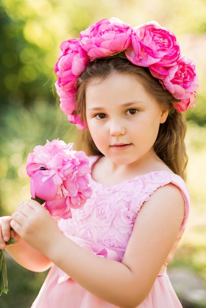 Foto retrato de uma menina com flores cor de rosa. uma coroa de peônias na cabeça da criança.