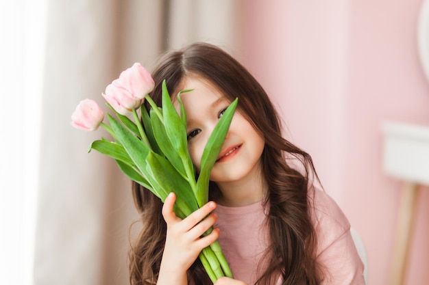 Retrato de uma menina com longos cabelos escuros closeup O bebê abraça um buquê de tulipas cor de rosa frescas e delicadas Um presente para o feriado de primavera