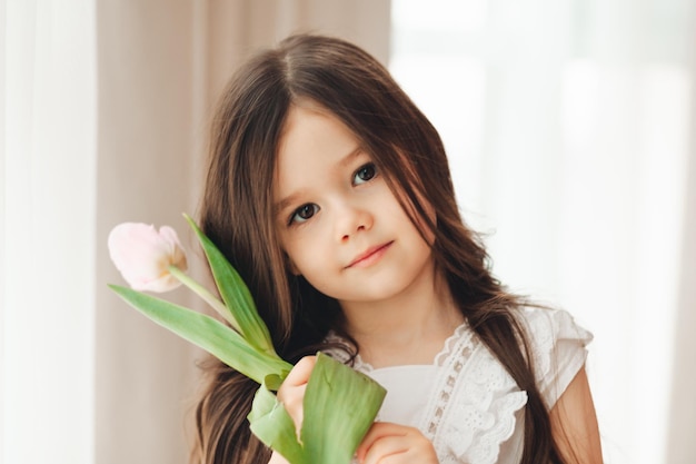 Retrato de uma menina com longos cabelos escuros closeup O bebê abraça um buquê de tulipas cor de rosa frescas e delicadas Um presente para o feriado de primavera