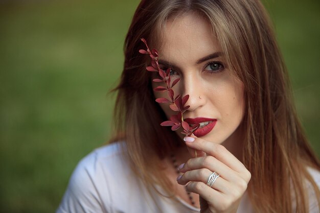 Retrato de uma menina com maquiagem brilhante e lábios Marsala com uma planta vermelha