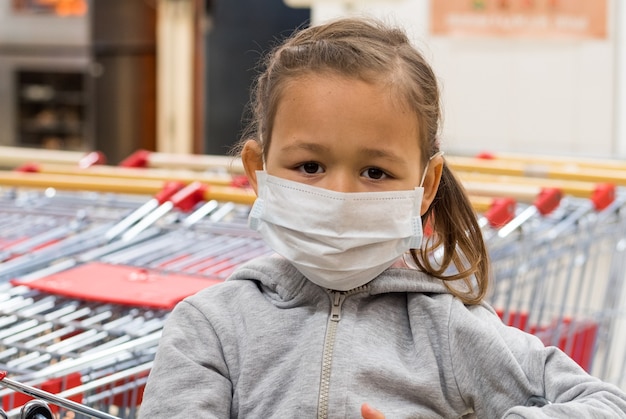 Foto retrato de uma menina com máscara médica olhando para a câmera no supermercado