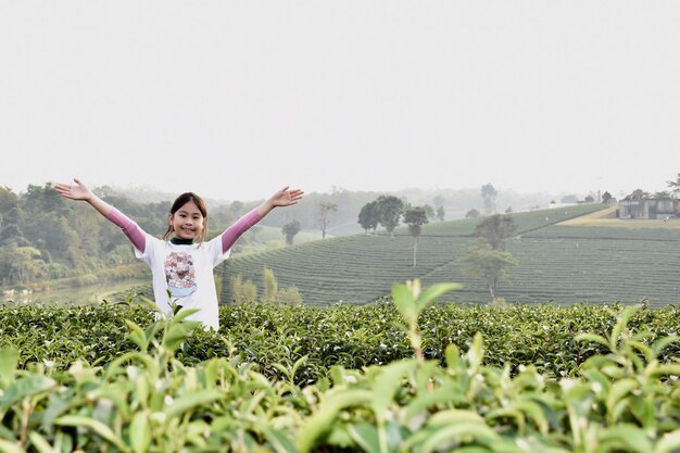 Foto retrato de uma menina com os braços estendidos de pé no meio de plantas no campo contra o céu claro