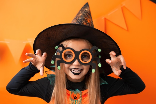 Foto retrato de uma menina com raiva em uma fantasia de bruxa em um fundo laranja. feliz dia das bruxas