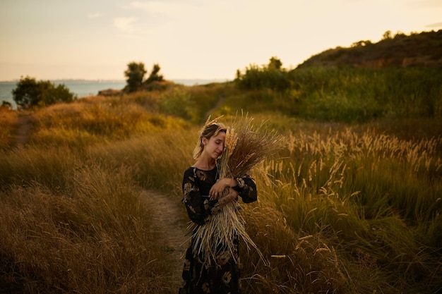 retrato de uma menina com um buquê de flores silvestres jovem atravessa o campo ao pôr do sol