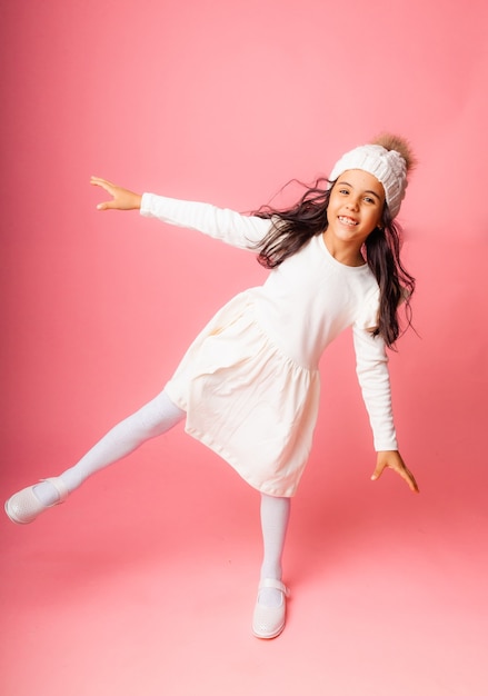 Foto retrato de uma menina com um chapéu branco de malha de inverno e um vestido branco em um fundo rosa