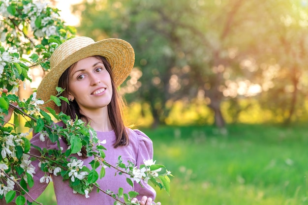 Retrato de uma menina com um chapéu de palha em um pomar de macieiras florescendo ao pôr do sol copyspace