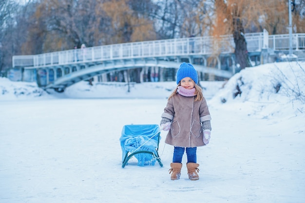 Retrato de uma menina com um trenó em um fundo de neve no parque