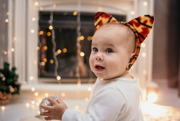 Retrato de uma menina com uma bandana e orelhas de tigre sentada no fundo de uma lareira festiva