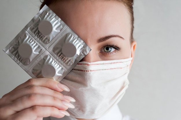 Foto retrato de uma menina com uma máscara médica segurando um pacote de pílulas na mão close upxa