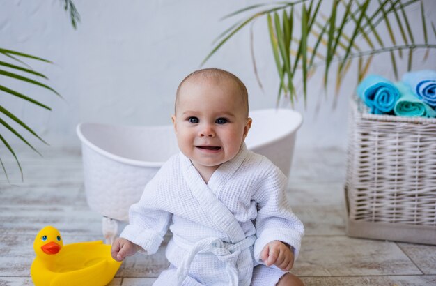 Retrato de uma menina com uma túnica branca, sentada perto de uma banheira, em um fundo branco com um lugar para texto. cuidado infantil