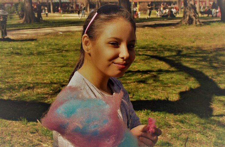 Foto retrato de uma menina comendo algodão doce enquanto está de pé no parque