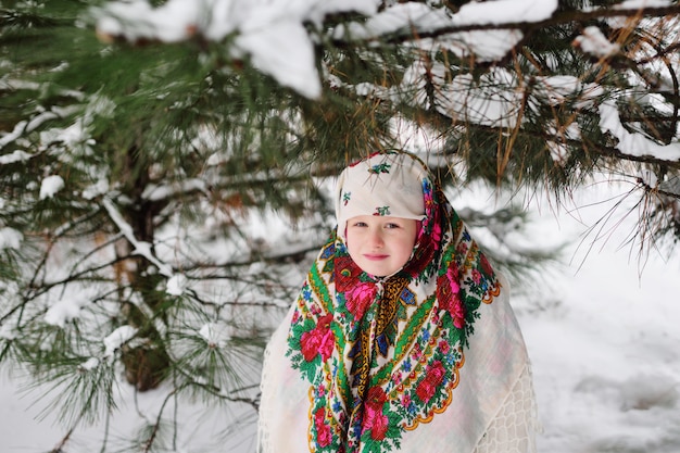 Retrato de uma menina criança em um lenço na cabeça no estilo Urs na superfície da neve e da floresta