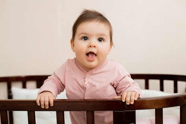 Retrato de uma menina criança sentada em casa em um berço de pijama