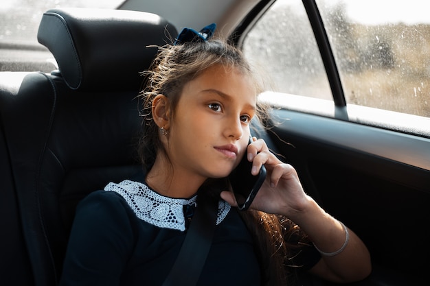 Retrato de uma menina da escola falando no smartphone no carro.