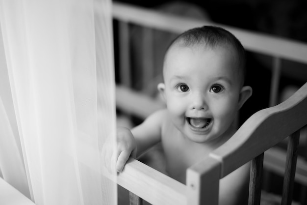 Retrato de uma menina de 5 meses em um berço em um berçário brilhante depois de dormir e olhar