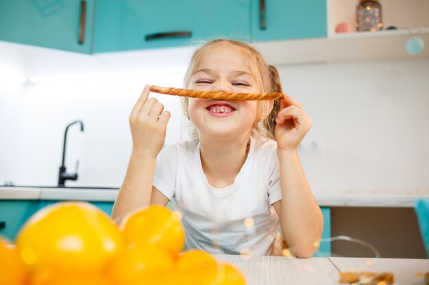 Retrato de uma menina de 7 anos de idade se senta na cozinha e brinca com palitos de pão. criança toma café da manhã na cozinha