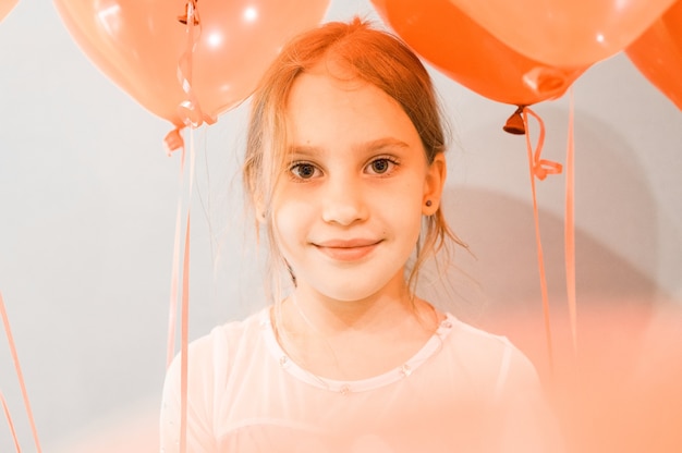 Retrato de uma menina de 8 anos de idade, caucasiana, sorridente, pequena e fofa, feliz, cândida, com balões vermelhos no contexto de uma parede cinza durante a celebração do aniversário dela em casa