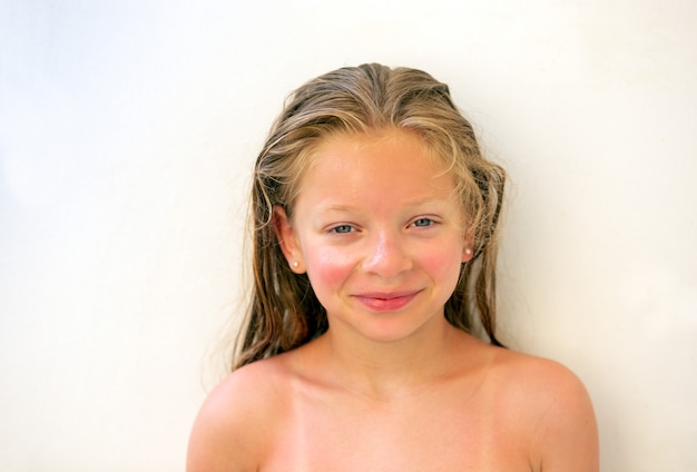 Foto retrato de uma menina de 9 anos com longos cabelos loiros molhados e olhos azuis, com queimaduras de sol