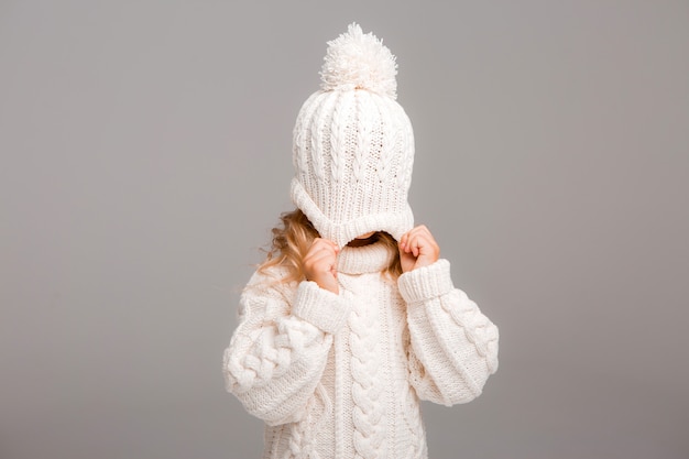 Retrato de uma menina de cabelos cacheados em um chapéu branco de malha de inverno