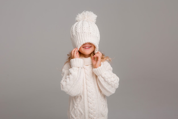 Retrato de uma menina de cabelos cacheados em um chapéu branco de malha de inverno