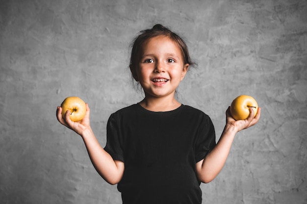 Retrato de uma menina de felicidade comendo uma maçã verde em fundo cinza. Saúde, comida saudável