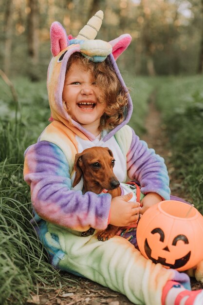 Foto retrato de uma menina e um dachshund anão em fantasias de halloween com uma cesta de abóbora para doces