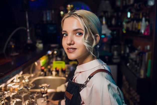 Retrato de uma menina em um bar à noite, atrás do balcão.