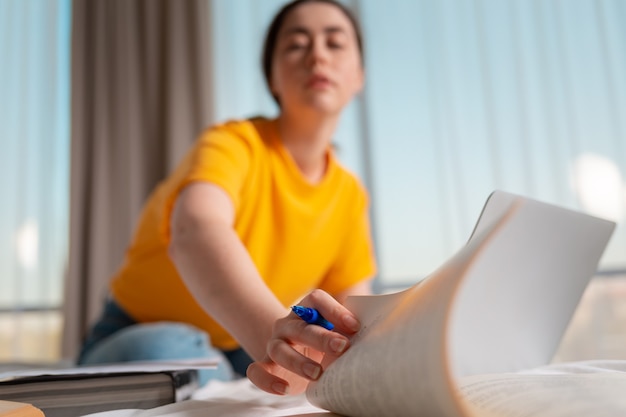 Retrato de uma menina em um borrão, folheia as páginas. Laptop e documentos estão lado a lado. Fechar-se. O conceito de cursos online e educação online.