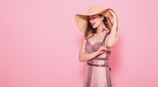 Retrato de uma menina em um chapéu de verão e vestido em uma parede rosa