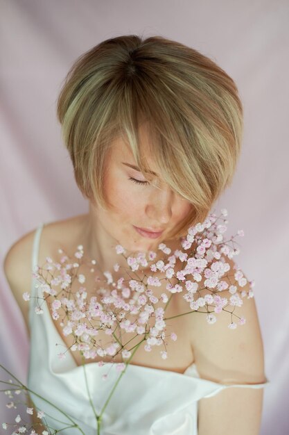 Retrato de uma menina em um fundo rosa com flores Ternura e feminina A esfera da beleza e saúde da mulher Corte de cabelo curto cabelo loiro