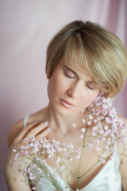 Retrato de uma menina em um fundo rosa com flores Ternura e feminina A esfera da beleza e saúde da mulher Corte de cabelo curto cabelo loiro