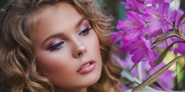 Retrato de uma menina em um jardim florescendo Um arbusto de flores é rododendro rosa Lindo cabelo e maquiagem