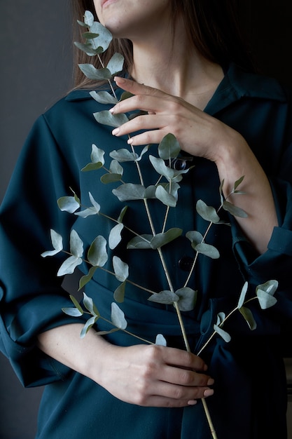 Retrato de uma menina em um vestido verde, segurando um galho de eucalipto em um fundo escuro