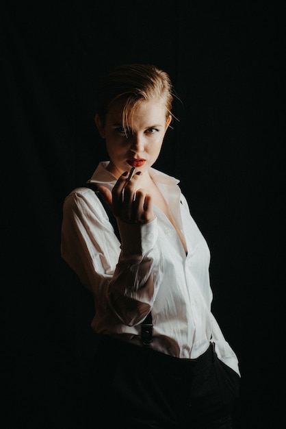 Retrato de uma menina em uma camisa branca e suspensórios, fumando um cigarro. foto com o grão jogado