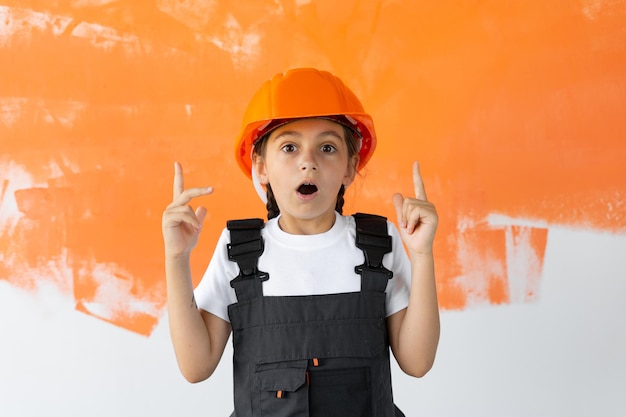 Retrato de uma menina encantadora com um capacete laranja na cabeça. dedo indicador erguido para cima emoção de surpresa.