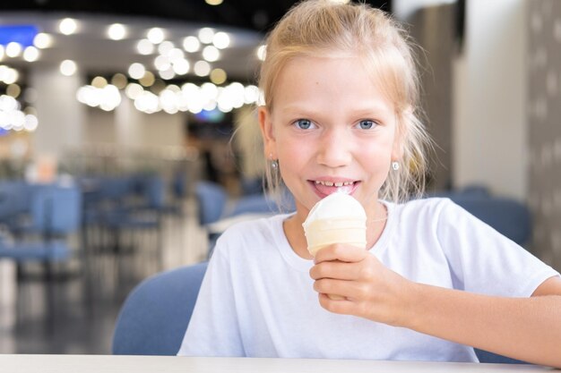 Retrato de uma menina engraçada com fome comendo sorvete frio e delicioso em uma xícara de waffle sentado em um fundo escuro de café