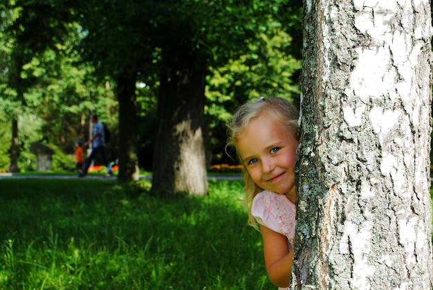 Foto retrato de uma menina escondida atrás de uma árvore no parque