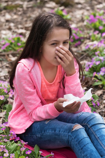 Foto retrato de uma menina espirrando enquanto está sentada em plantas com flores