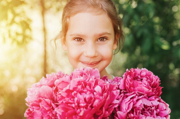 retrato de uma menina feliz caucasiana de sete anos de idade, segurando nas mãos um buquê de peônia rosa