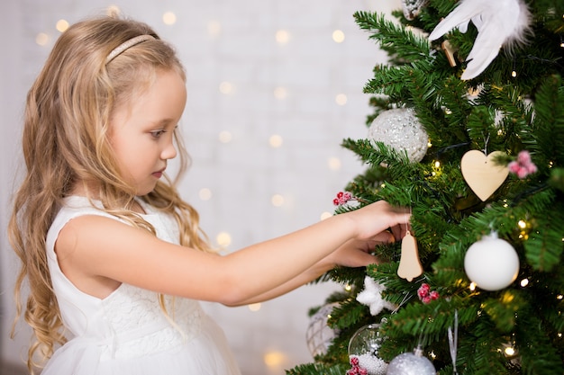 Retrato de uma menina feliz e fofa decorando a árvore de Natal em casa