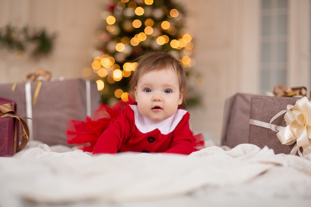 Retrato de uma menina feliz em uma camisola de malha vermelha com uma caixa de presente de Natal perto da árvore de Natal