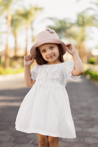 Foto retrato de uma menina feliz em vestido boho branco e chapéu de palha no fundo das palmeiras