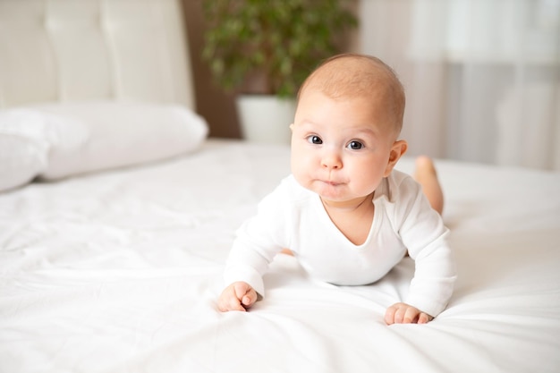 Retrato de uma menina fofa de 5 meses em uma roupa branca em uma cama branca Espaço para texto Criança