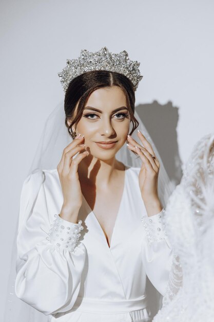 Foto retrato de uma menina incrivelmente bonita noiva em um roupão branco no quarto a noiva posa na manhã antes da cerimônia de casamento