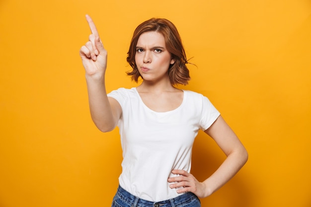 Retrato de uma menina insatisfeita de pé isolado na parede amarela, gesticulando