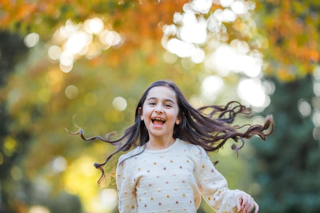 Retrato de uma menina linda de 9 anos com longos cabelos escuros em roupas brilhantes criança feliz no parque de outono