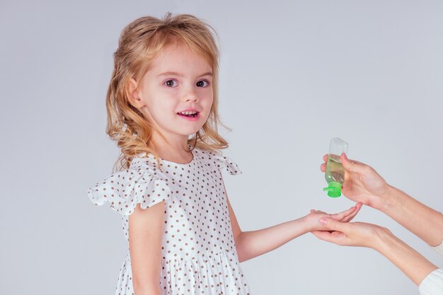 Retrato de uma menina loira bonitinha aplicando gel anti-séptico antibacteriano nas mãos vírus anti-bactérias em estúdio em fundo branco. proteção de epidemia de bebê, mão da mãe close-up.