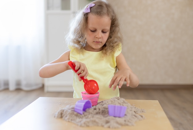 Retrato de uma menina loira brincando com areia cinética em casa