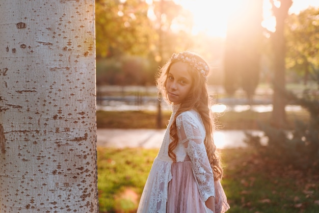 Retrato de uma menina loira com cabelo encaracolado com vestido de comunhão ao pôr do sol
