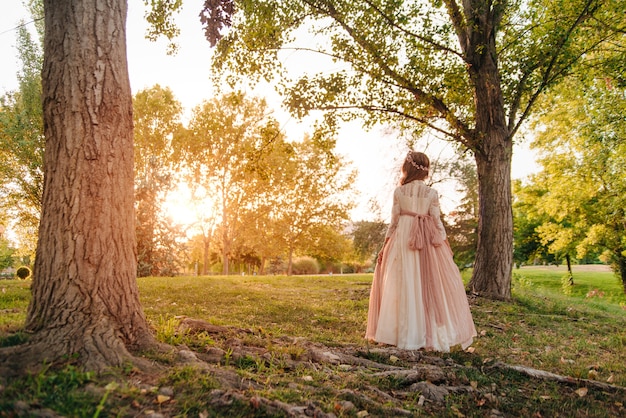 Foto retrato de uma menina loira com cabelo encaracolado com vestido de comunhão caminhando por entre algumas árvores